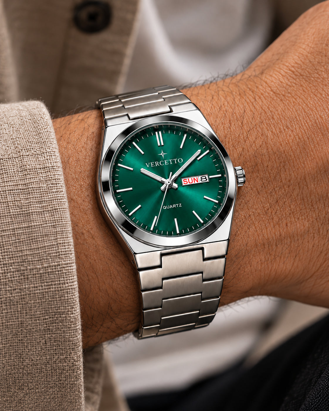 Propuesta VERCETTO: primer plano del reloj verde esmeralda en una muñeca con manga beige, brazalete sin grabado y firma en la esfera